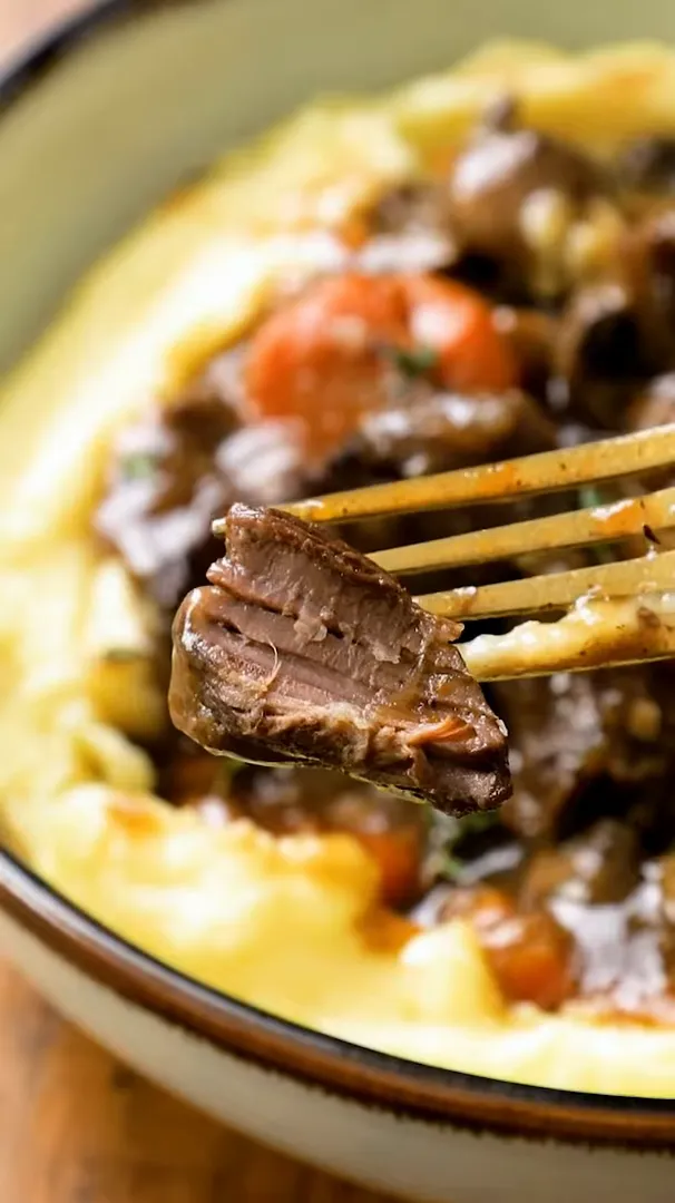 Fork holding a forkful of seared beef over mashed potatoes and beef bourguignon, showing the browned exterior and tender interior.