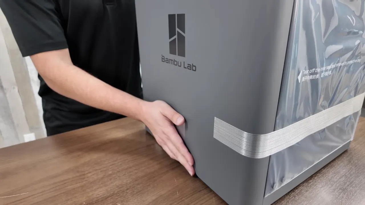 Bambu Lab P2S side with logo and hand demonstrating the integrated handle during unboxing.