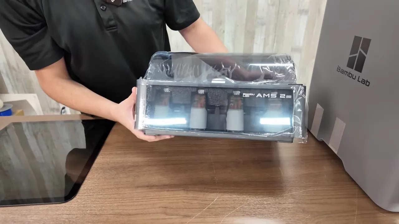 Clear front view of AMS2 Pro module in protective film next to Bambu P2S