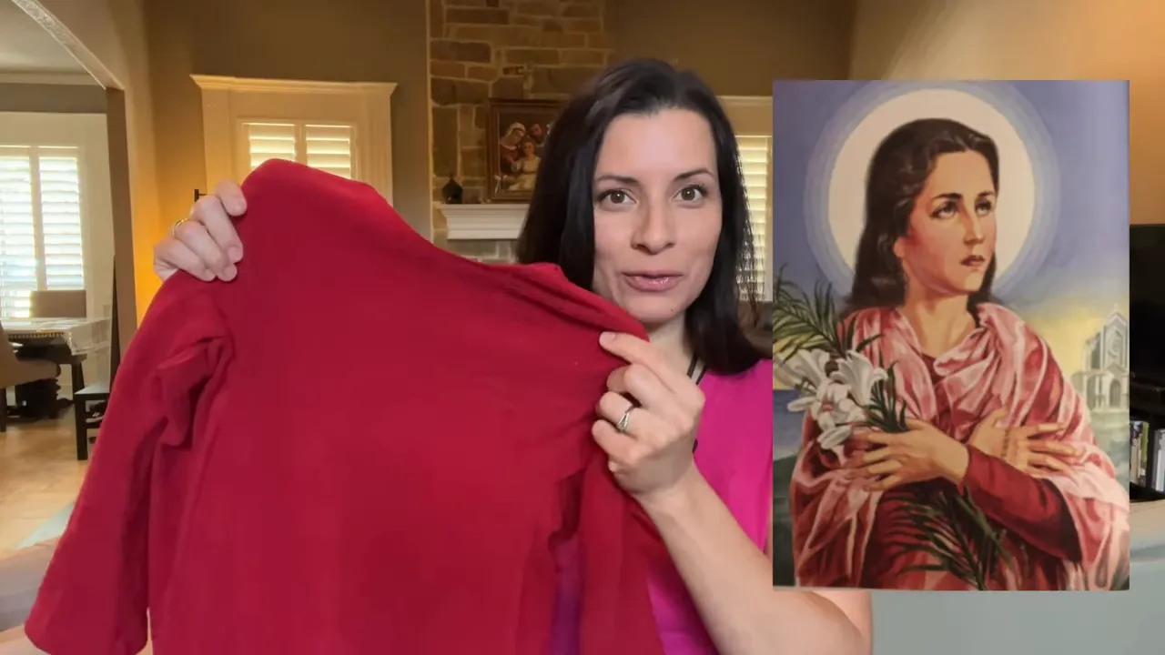Woman holding up a red fleece tunic beside an image of St. Maria Goretti