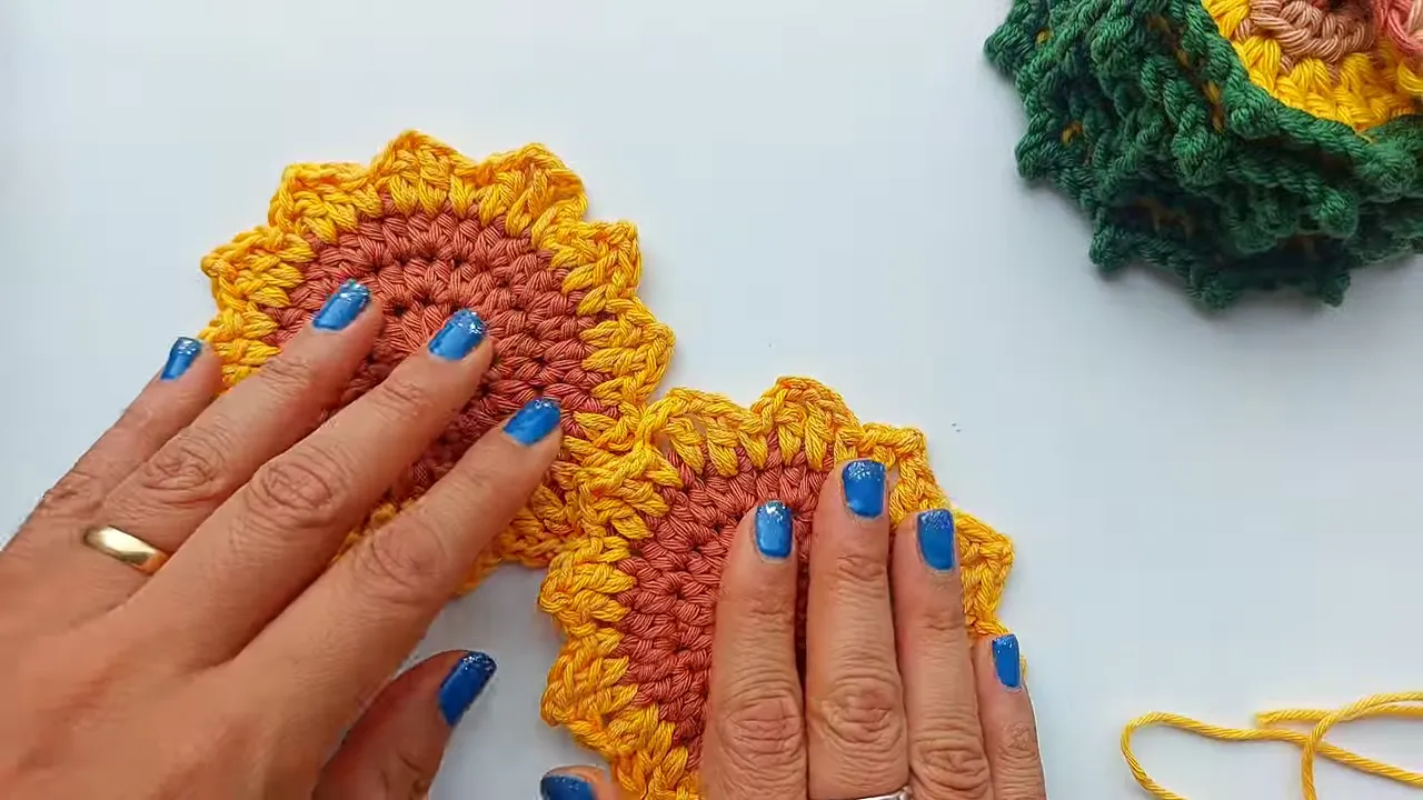 Two crochet sunflower motifs with brown centers and yellow petals laid side by side