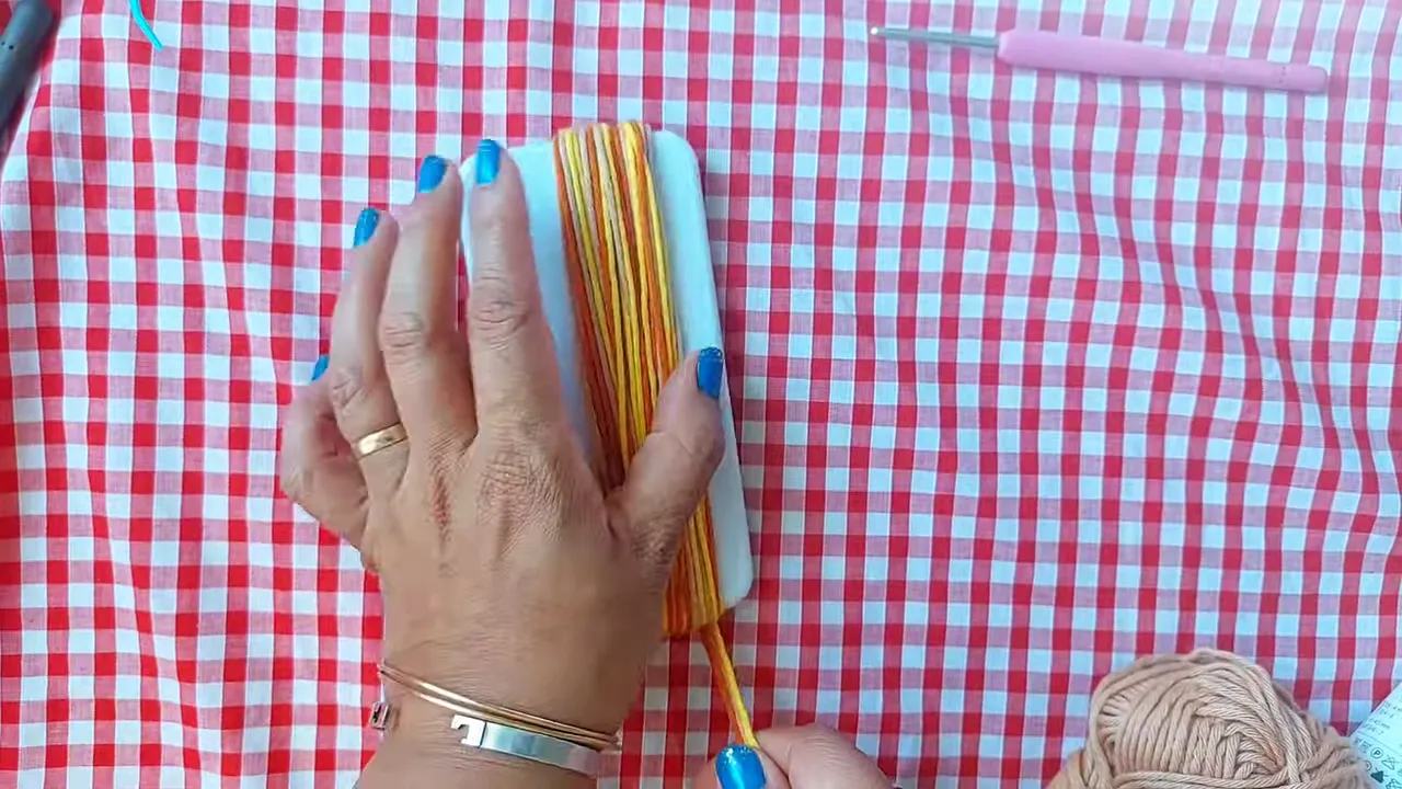 Beige, yellow, and orange yarn wrapped around a small white rectangular object on a red checked surface
