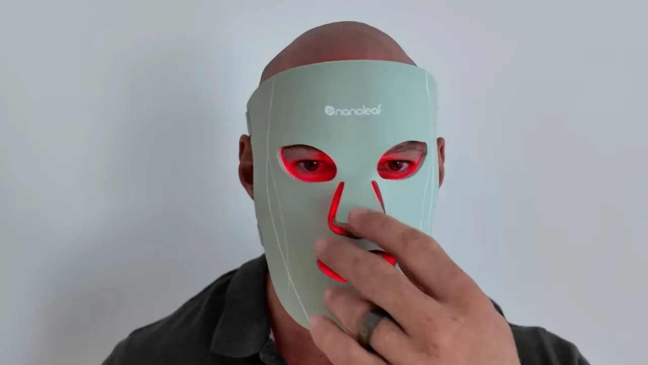 Reviewer wearing LED face mask adjusting the nose area with hand; red LEDs visible through cutouts