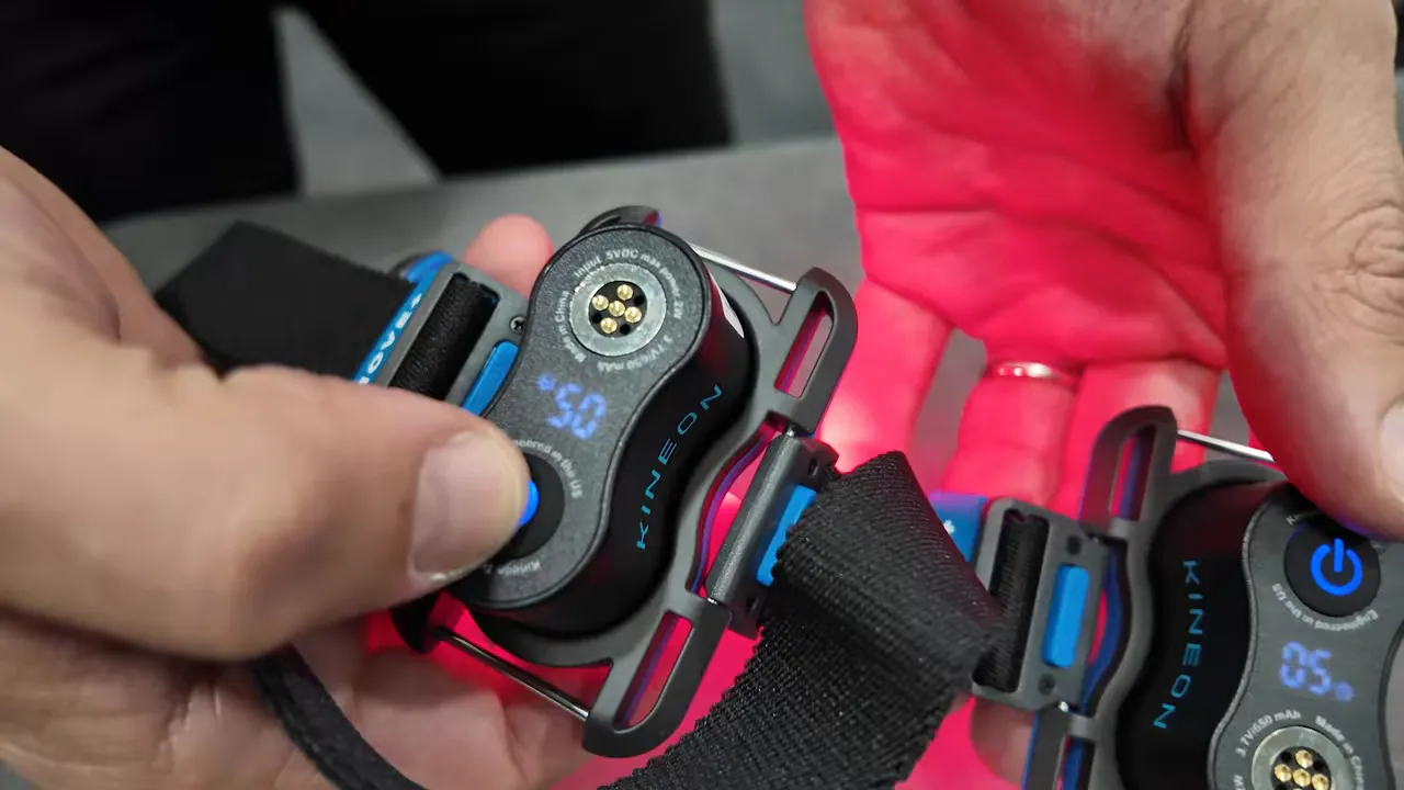 Hands holding Kineon Move Plus module with illuminated LED time display, connector pins and strap.