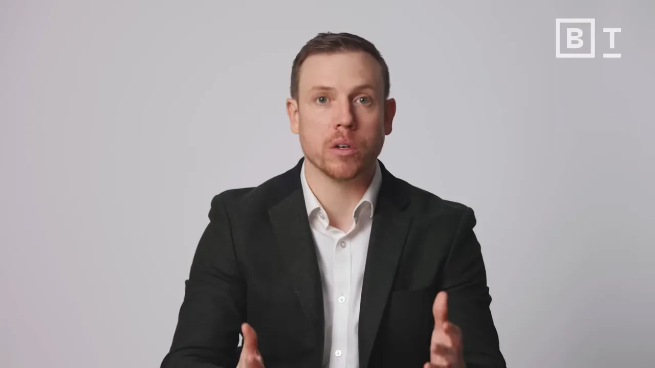 Well-composed medium shot of presenter speaking with hands visible, neutral background and BT logo.