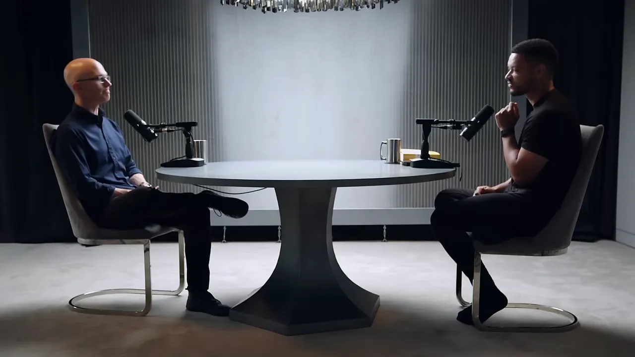 Two people seated at a round table during a podcast interview with microphones