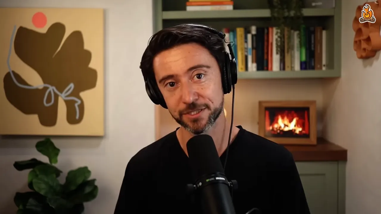 Podcast host speaking into a microphone with bookshelf, plant, and small fireplace in the background