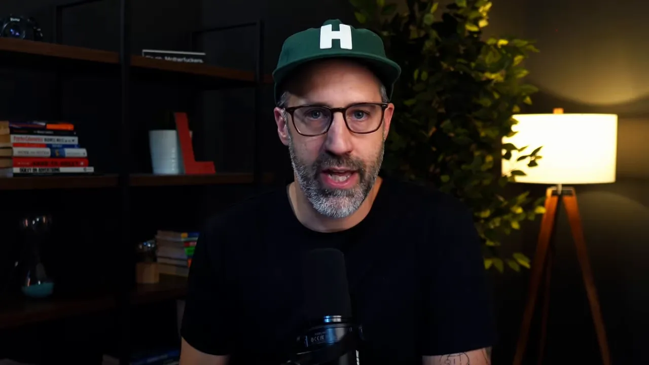 Host speaking clearly to camera with microphone, bookshelf and lamp in background