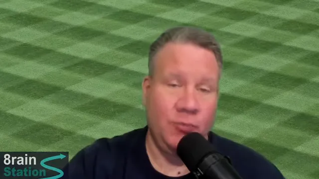 Speaker gesturing while speaking into a microphone against a green patterned background