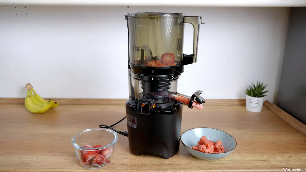 Kuvings AUTO10S mit gefrorenen Erdbeeren im Hopper und ausgegebenen Erdbeersorbet-Stücken in einer Schüssel.