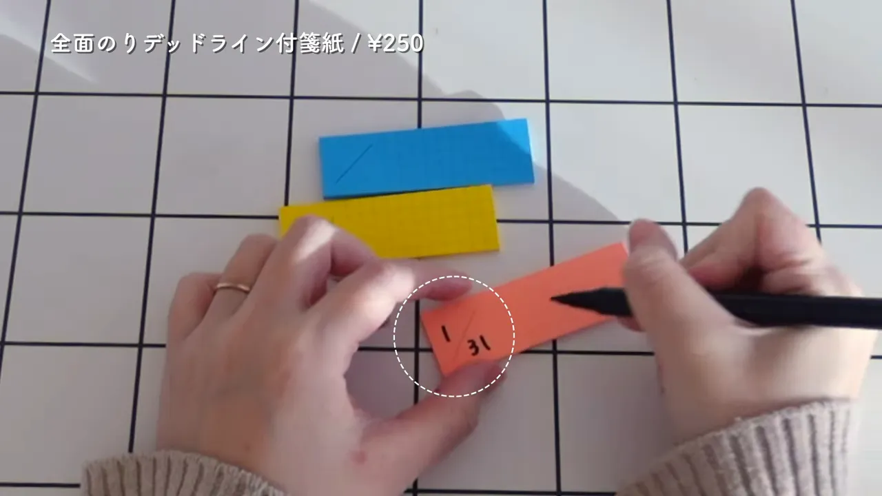 青・黄・オレンジの付箋が並び、オレンジの付箋に書き込み準備をしている手元