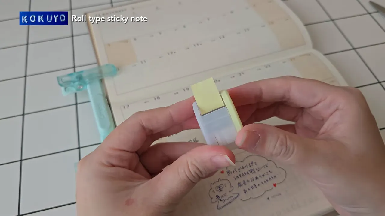 手帳を背景にロールふせんを引き出している手元のアップ写真（テープが見えている）