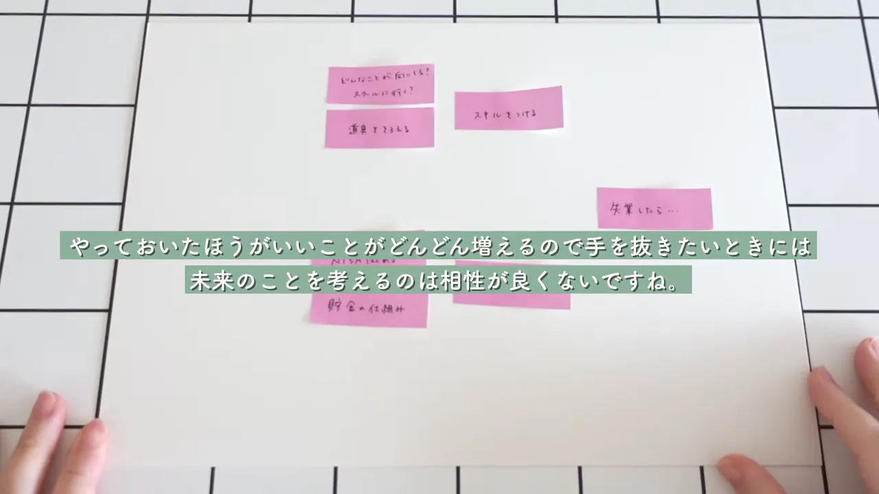 白いボード上にピンクの付箋が並んでいる俯瞰ショット。画面中央に緑の字幕で未来への不安を手放す旨のテキストが重なっている。