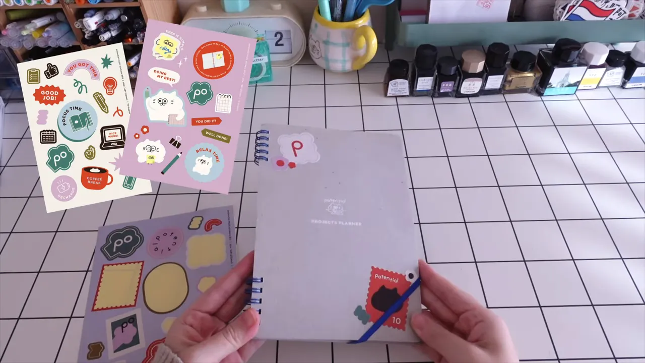 複数のシールシートとグレーのノートを持つ手元のクローズアップ写真