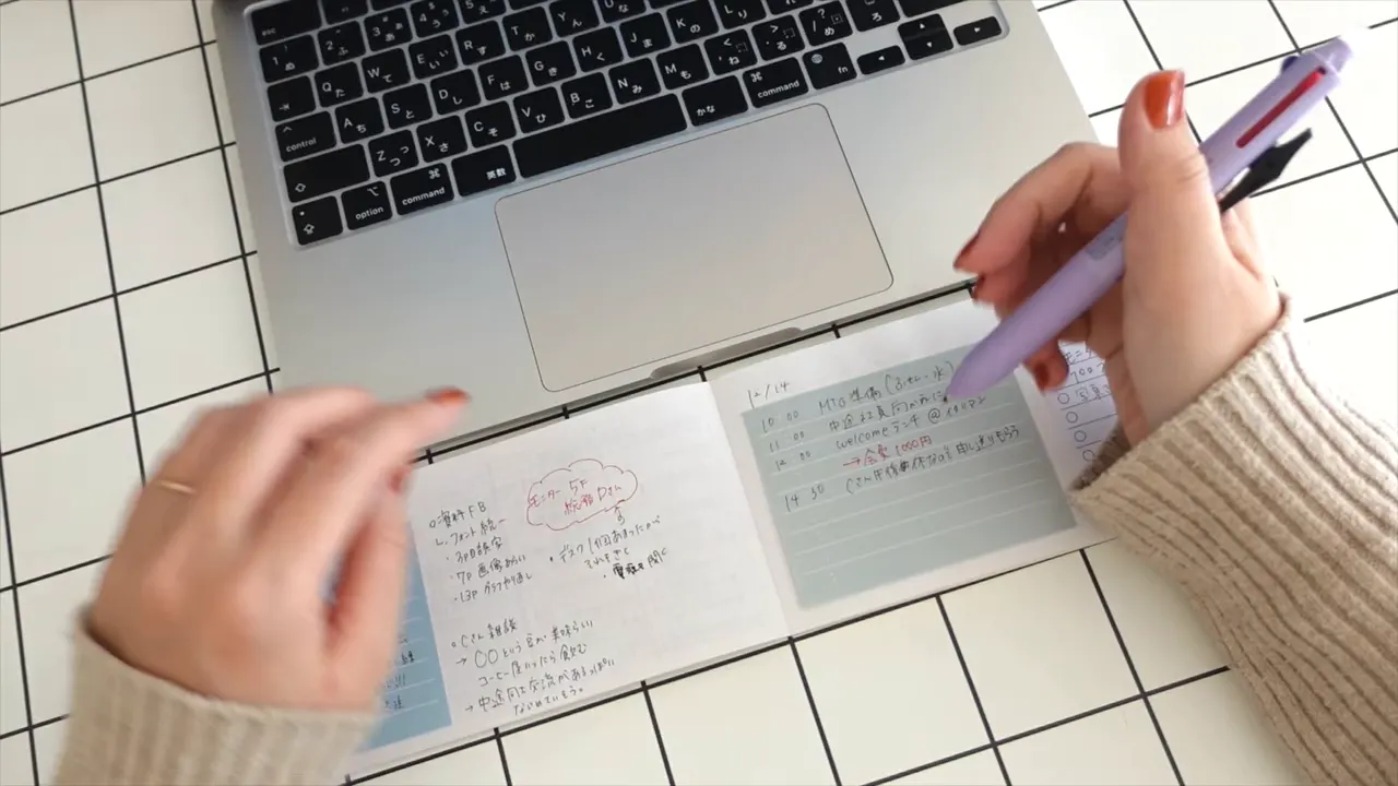 ノートパソコンの手前に横長ノートを広げてメモを書く手元