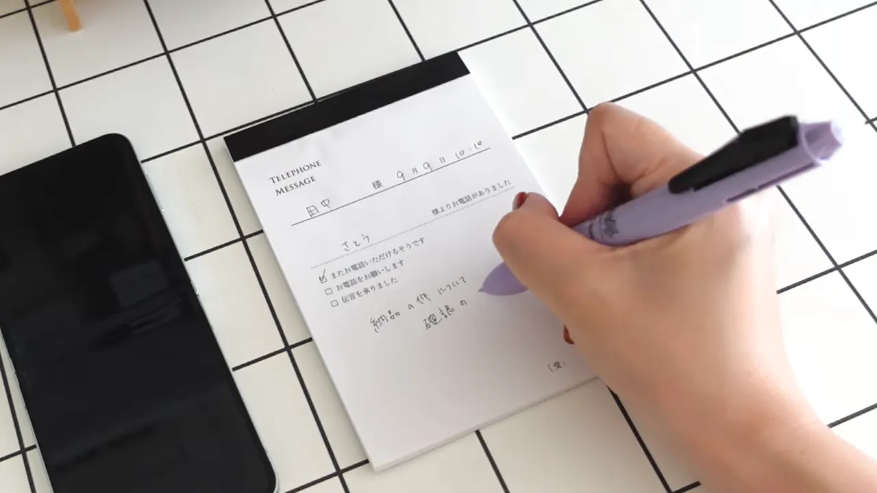 スマートフォンの通話画面の横で電話伝言メモに書き込む手元