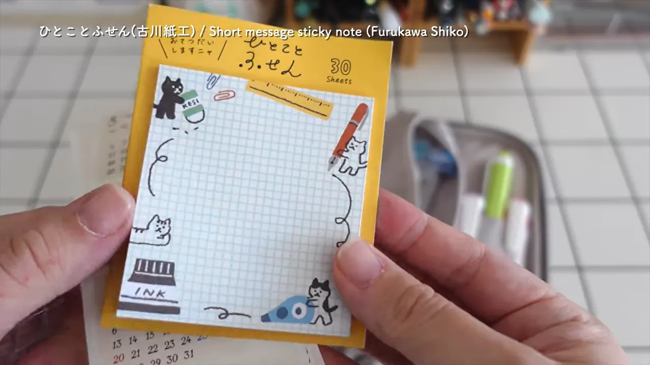 黄色い台紙に入った猫柄のひとことふせんを手に持っている
