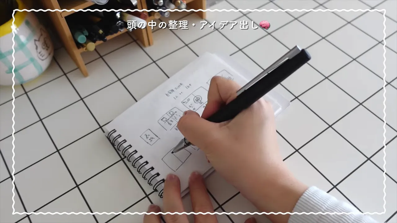 リングノートに黒いファインライターペンで図や文字を書いている手元