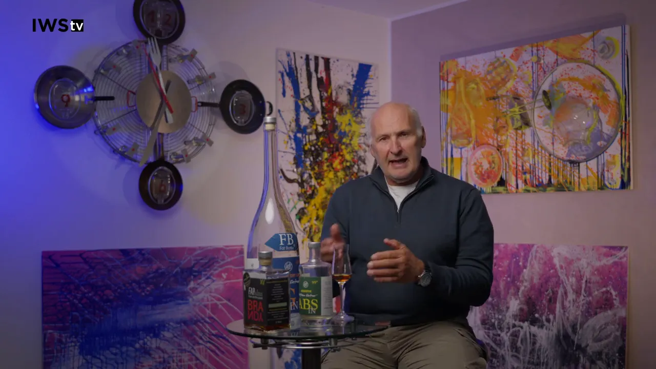 Sprecher gestikuliert vor bunten Bildern, Cognac-Flaschen und Nosing-Glas im Vordergrund