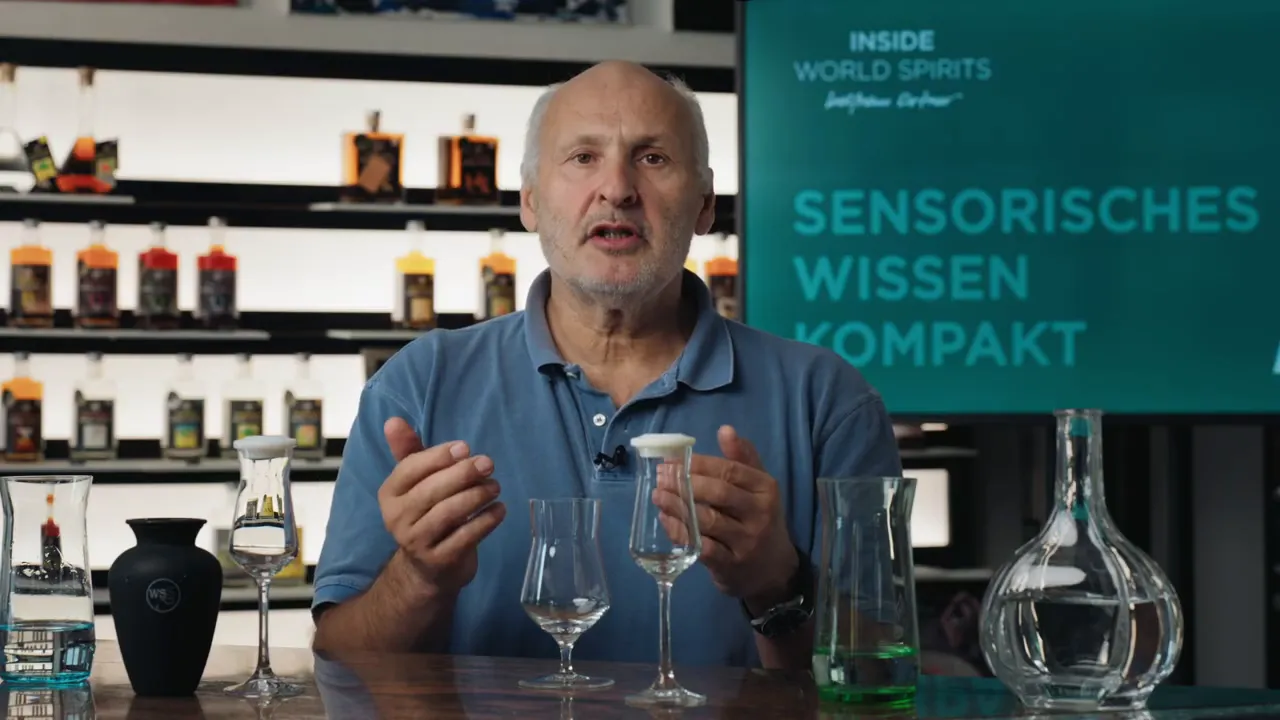Moderator gestikuliert erklärend vor mehreren Verkostungsgläsern; im Hintergrund ein Bildschirm mit 'Sensorisches Wissen Kompakt'.