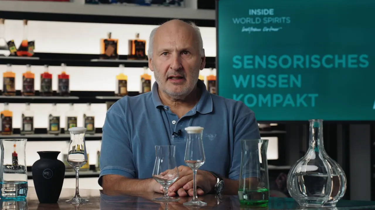 Moderator sitzt hinter einem Tisch mit verschiedenen Verkostungsgläsern; im Hintergrund 'Sensorisches Wissen' auf Display.
