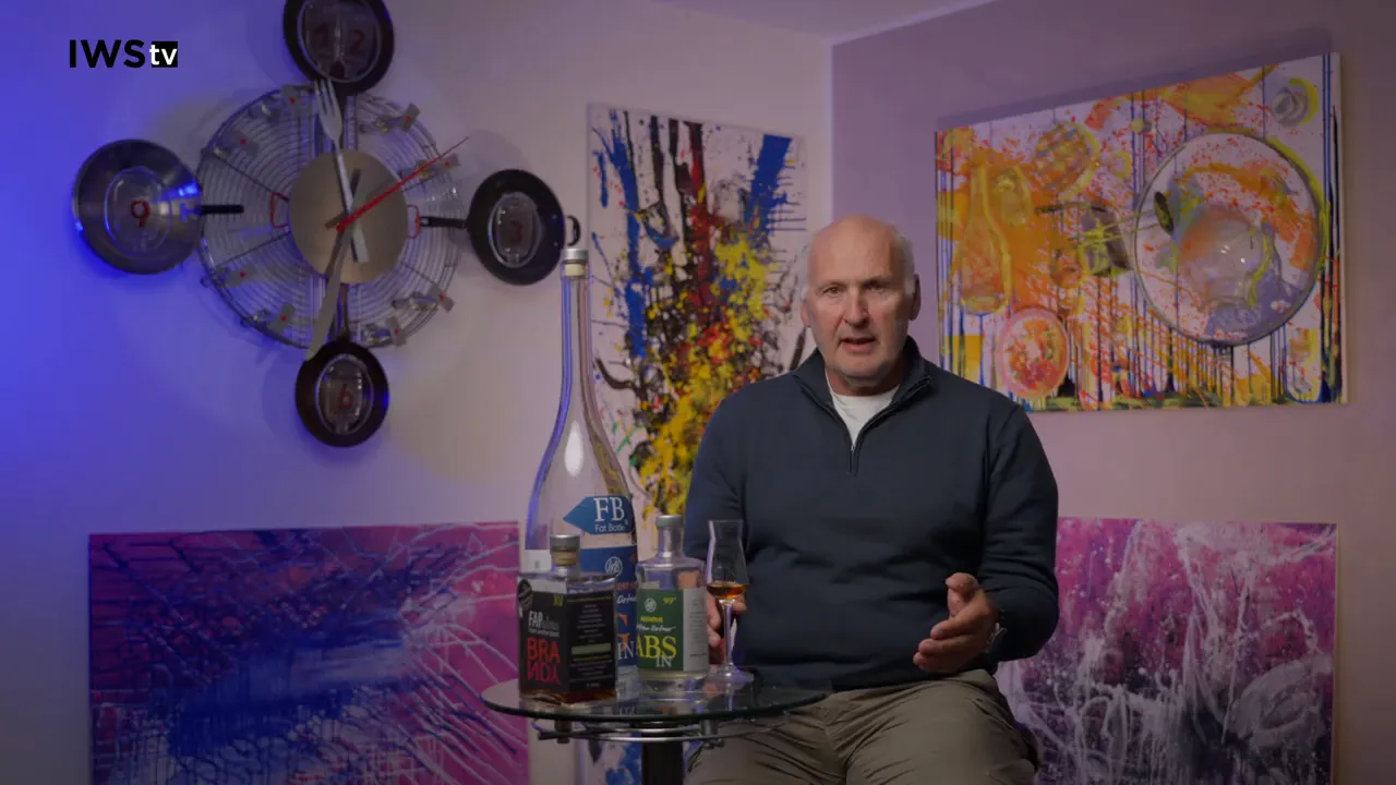 Moderator frontal sitzend, deutlich sichtbares Verkostungsglas und Flaschen auf dem Tisch