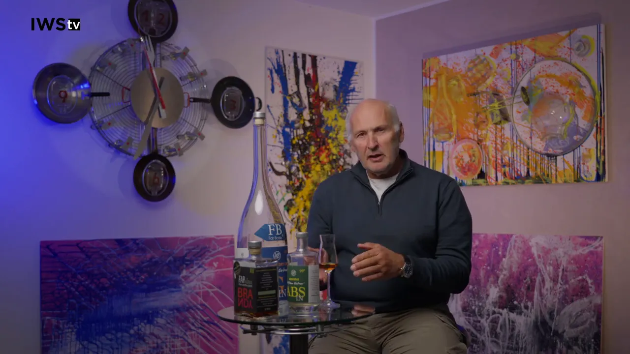 Moderator erklärt vor mehreren Flaschen und einem Glas auf einem Tisch, Kunst im Hintergrund