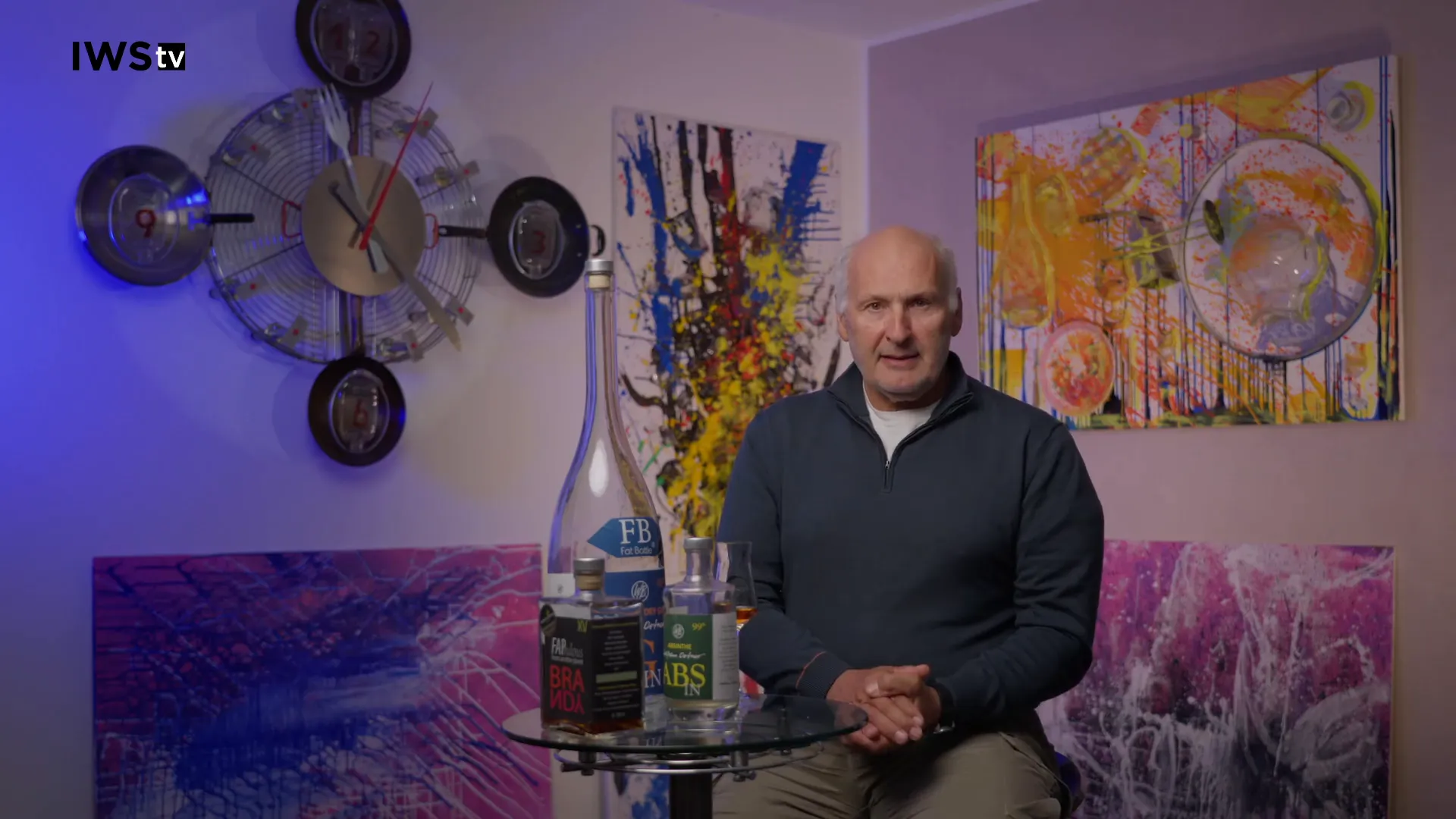 Sprecher neben einer Auswahl an Cachaça-Flaschen auf einem Glastisch, klare Darstellung verschiedener Abfüllungen.