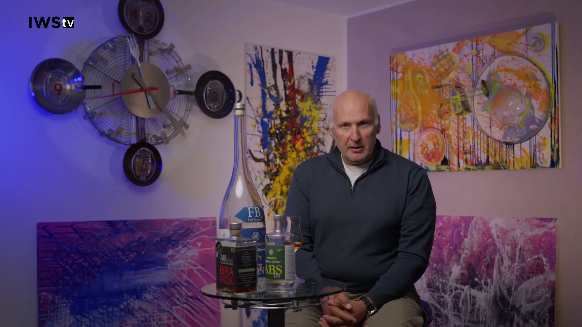 Moderator erklärt Cachaça neben Flaschen auf einem Glastisch vor bunten Bildern