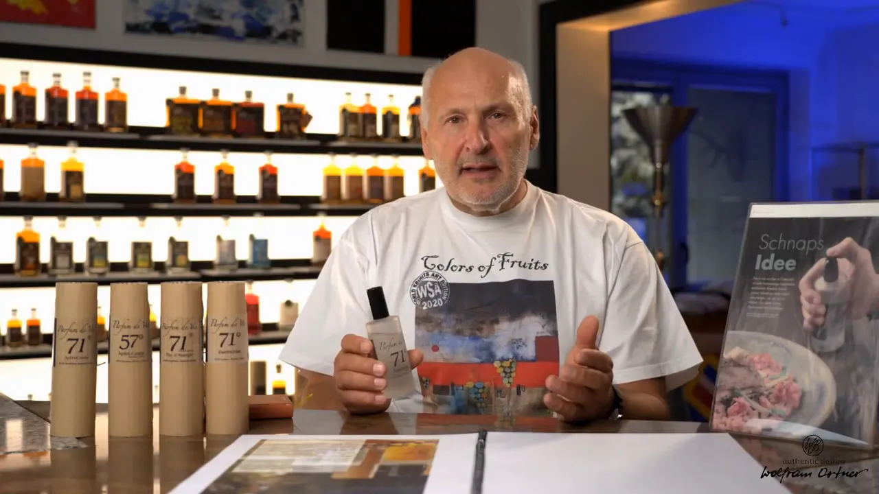 Table display of Parfum de Vie distillate tubes and a presenter holding a bottle, with a recipe/serving board visible to the right.