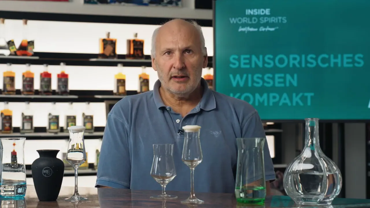 Moderator frontal mit mehreren Verkostungsgläsern auf dem Tisch und gut lesbarem Hintergrund 'Sensorisches Wissen Kompakt'.