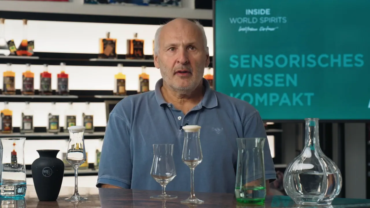 Referent sitzt mittig hinter drei Verkostungsgläsern und einem Dekanter; im Hintergrund 'Sensorisches Wissen' Display erkennbar.