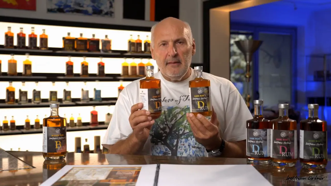 Presenter holding two ten‑year RUM MANIA bottles side-by-side with a lineup of bottles on the table and backlit shelves behind.