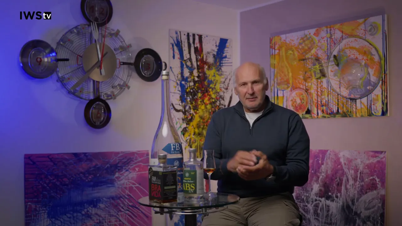 Mann erklärt mit Flaschen und Glas auf einem kleinen Glastisch im Vordergrund