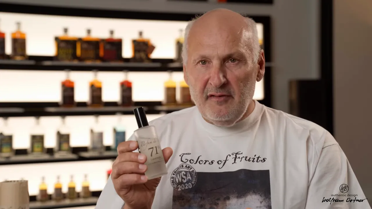 Hand hält Parfum de Vie 71 Flasche vor Regal mit Destillaten