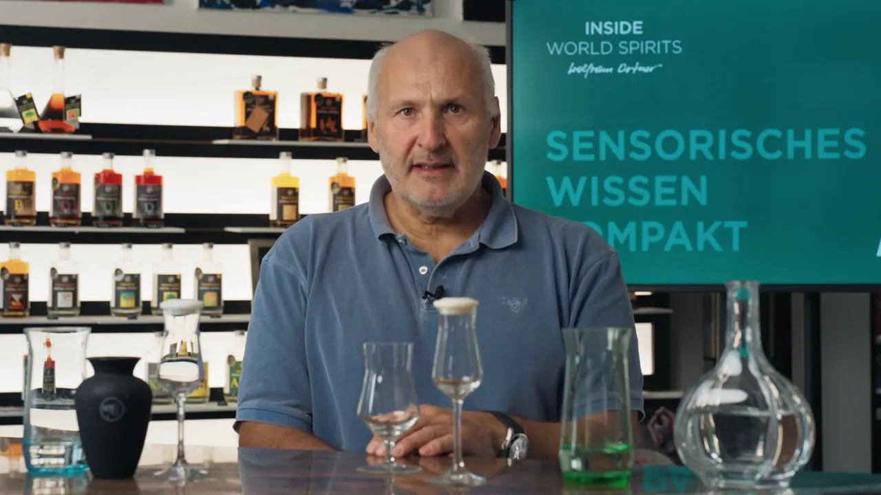 Moderator vor Regal mit Spirituosen und Bildschirm 'Sensorisches Wissen', mehrere Verkostungsgläser auf dem Tisch
