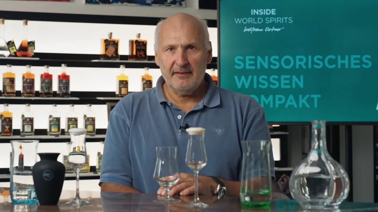 Moderator vor Schriftwand ‚Sensorisches Wissen‘, im Vordergrund Nosing-Gläser und Dekanter