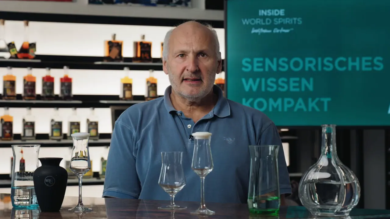 Mann im Studio hinter Verkostungsgläsern und Dekanter, Regal mit Flaschen im Hintergrund