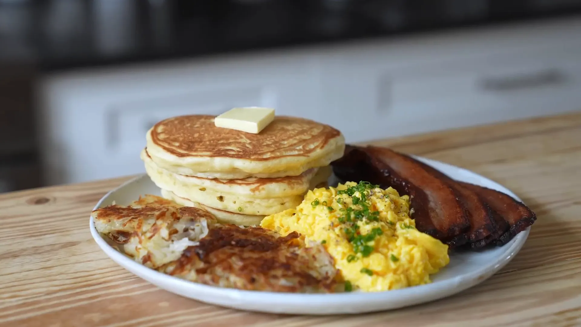 Plated American breakfast with pancakes, eggs, hash browns, and bacon