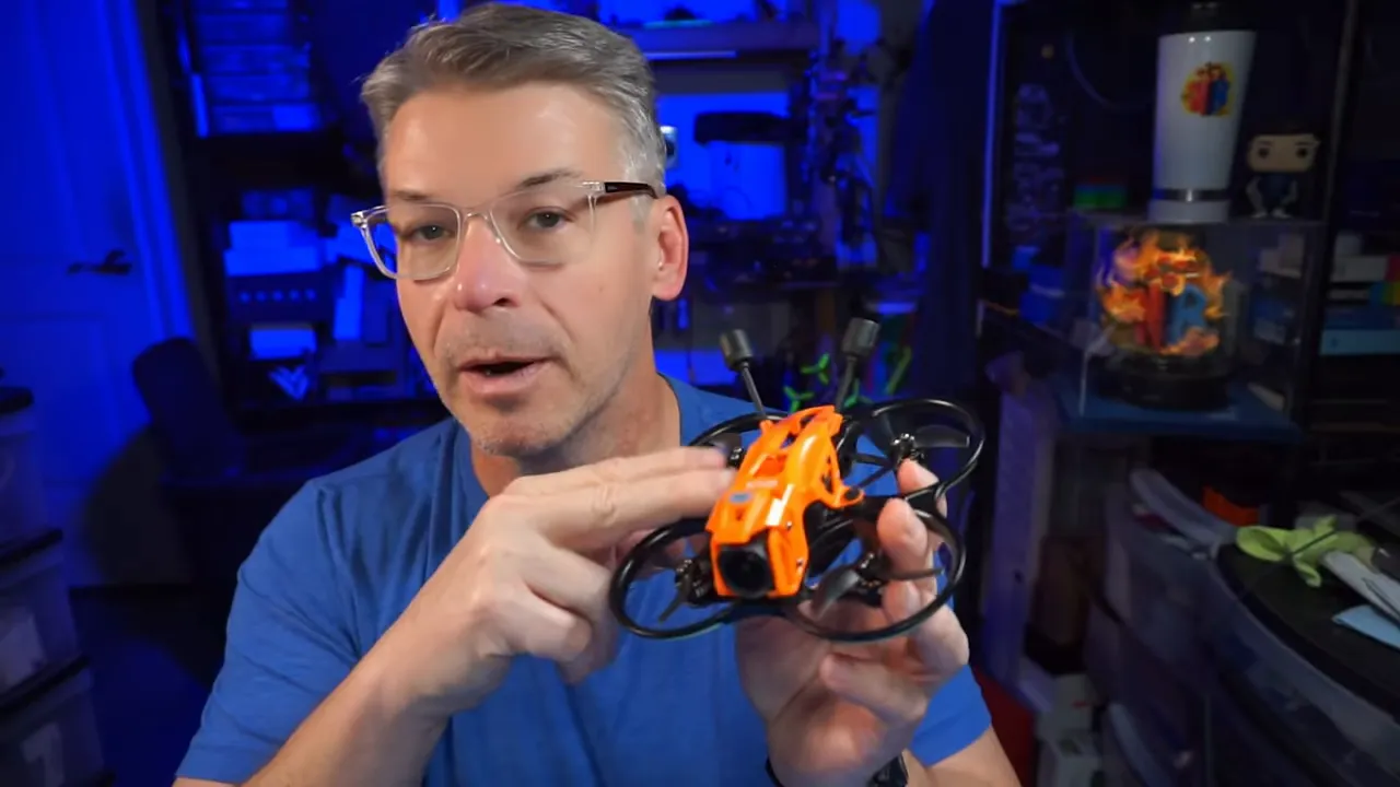 Person holding a DarkStar22 O4 Pro micro whoop with orange floating canopy and visible front camera in a workshop