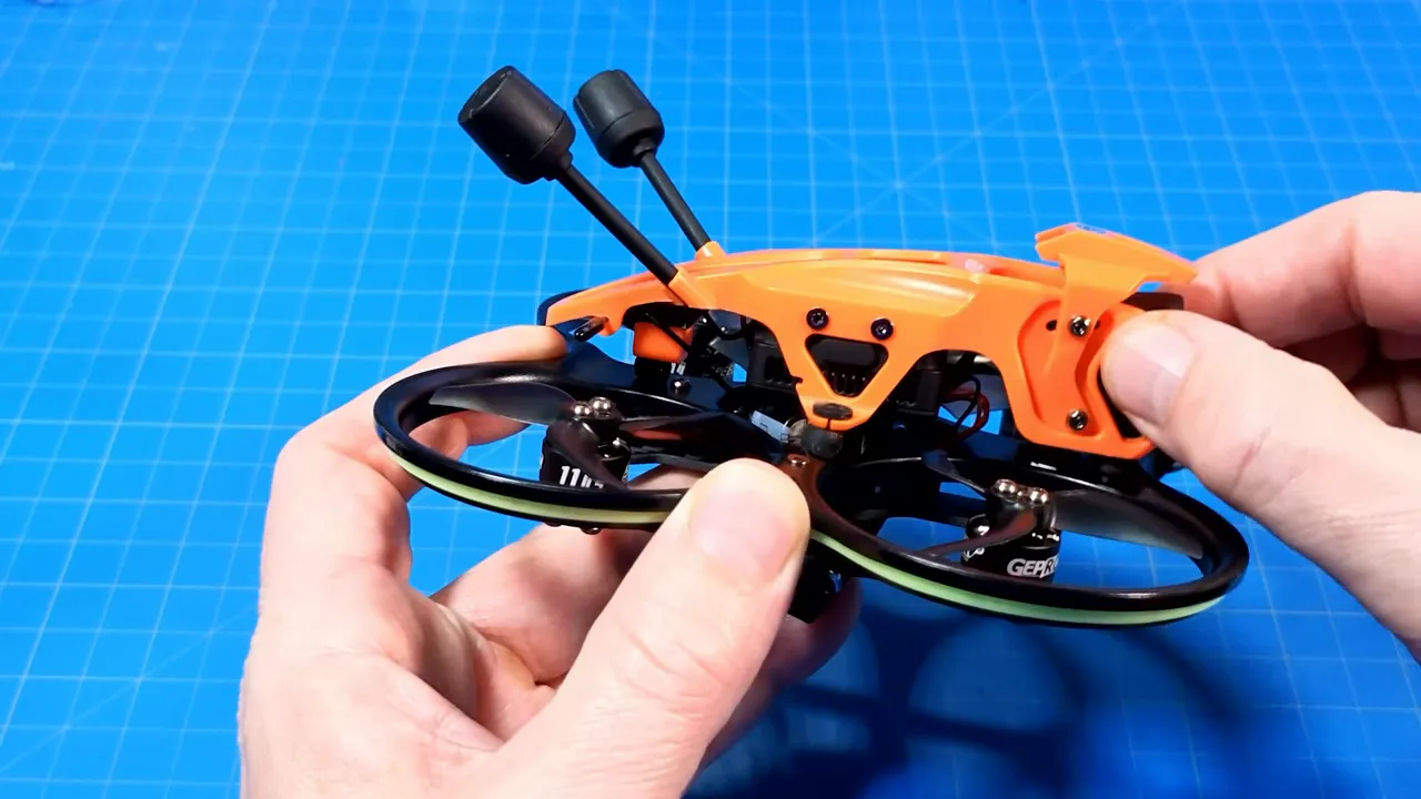 Hands holding a DarkStar22 micro whoop while adjusting the orange floating canopy and canopy screws on a blue work mat