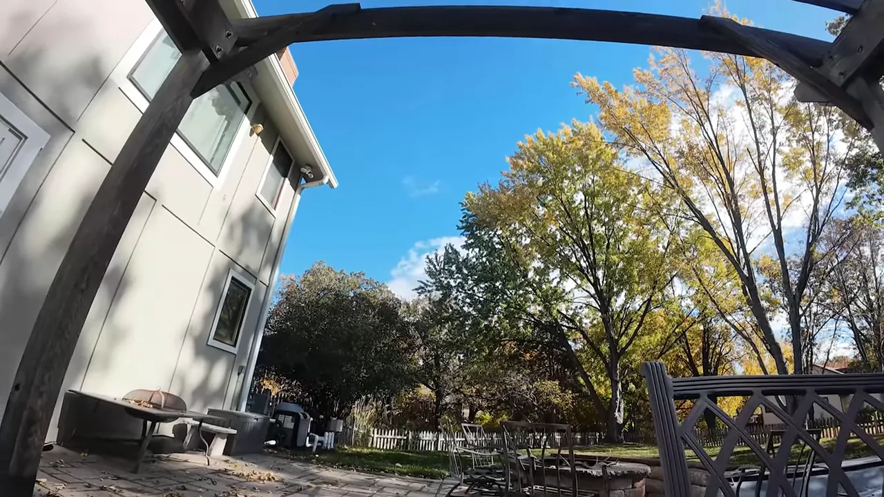 POV backyard/patio shot from the DarkStar22 showing pergola framing, patio furniture and tall trees with clear sky — a clean example of footage Rocksteady improves.