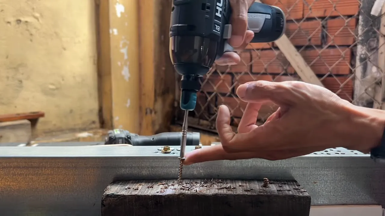 Máy Hucan đang siết vít vào gỗ, ngón tay làm thước đo vị trí vít