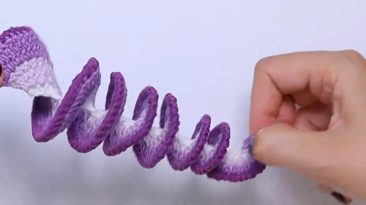 Hands holding an extended purple crochet spiral with a white inner section