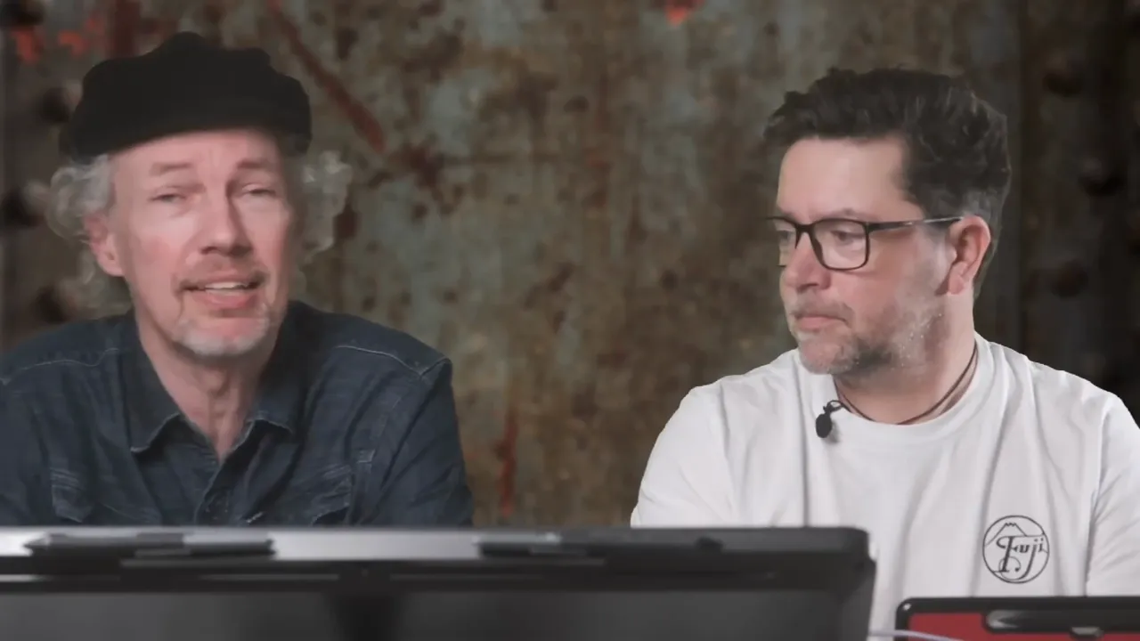 Twee sprekers aan een tafel over AI voor fotografen, met een laptop en microfoon tijdens de video