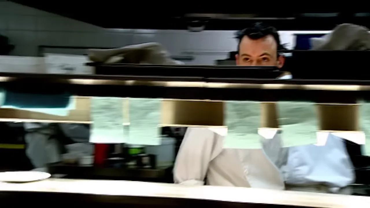 chef peeking over the pass with multiple order tickets hanging from the heat lamp