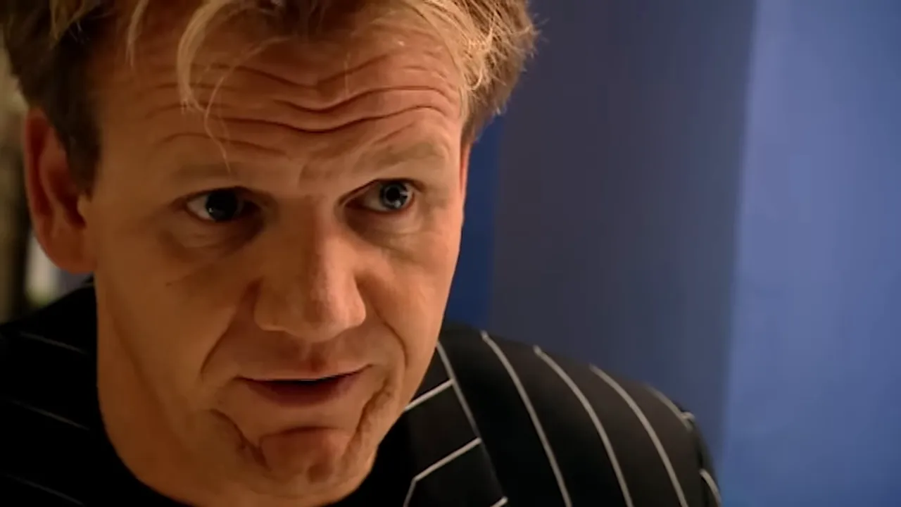 Close-up of a chef with an intent, attentive expression as they evaluate a dish against a blue background.