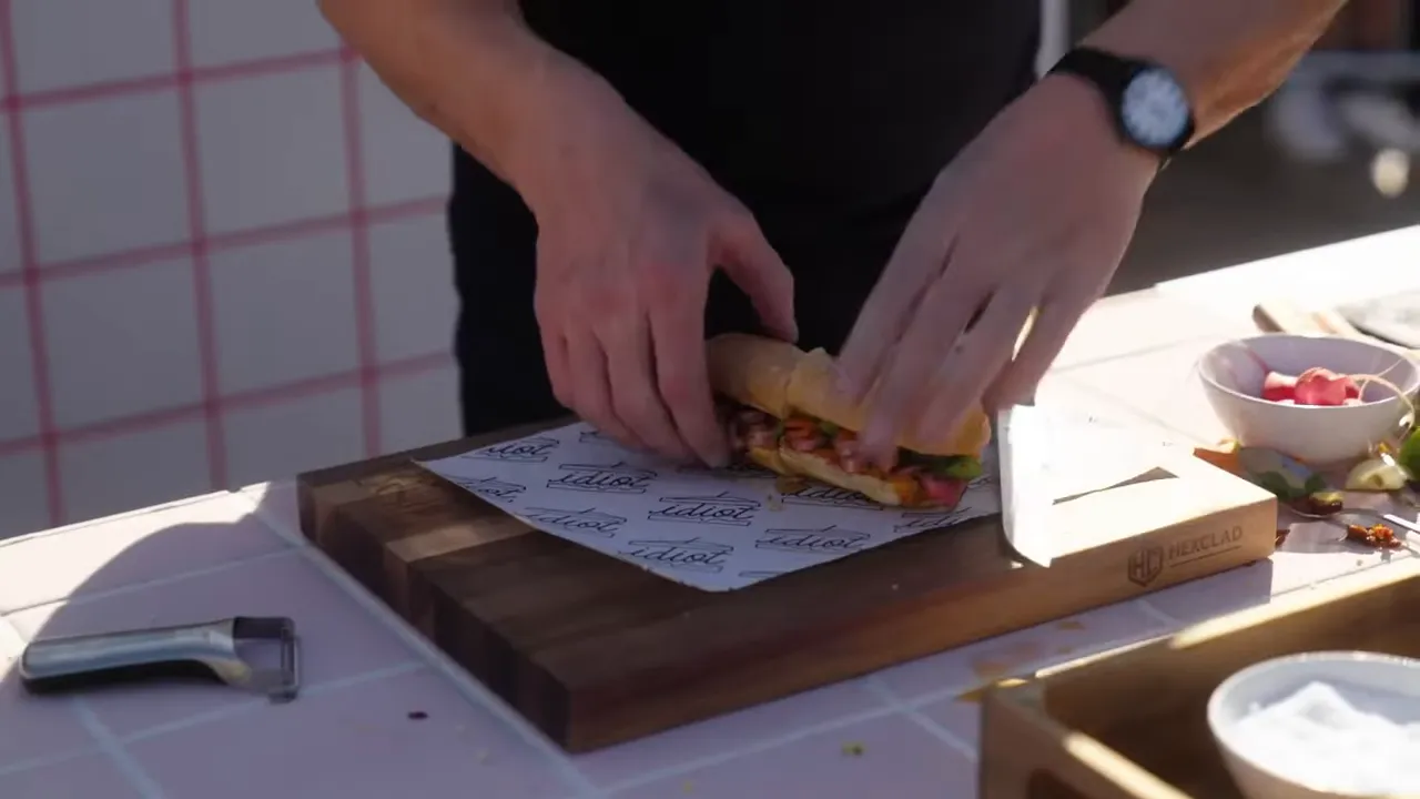 Close-up of hands assembling and wrapping a sandwich on a wooden cutting board with parchment