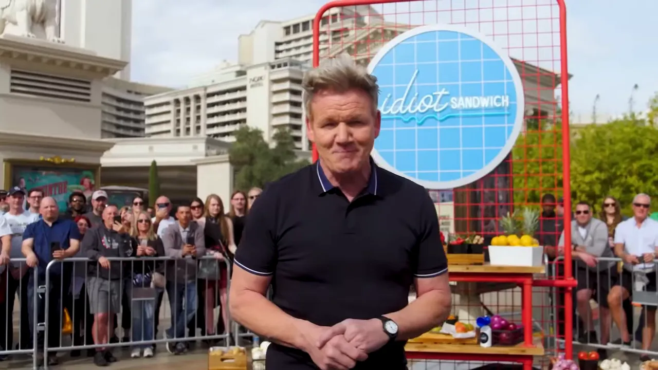 Presenter standing on an outdoor sandwich stage with a crowd and large round show sign behind