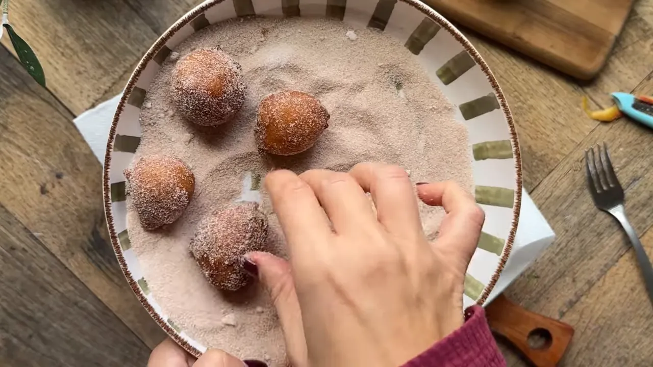 Freshly fried apple fritters being tossed in cinnamon sugar